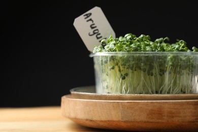 Photo of Sprouted arugula seeds in plastic container on wooden table, closeup. Space for text