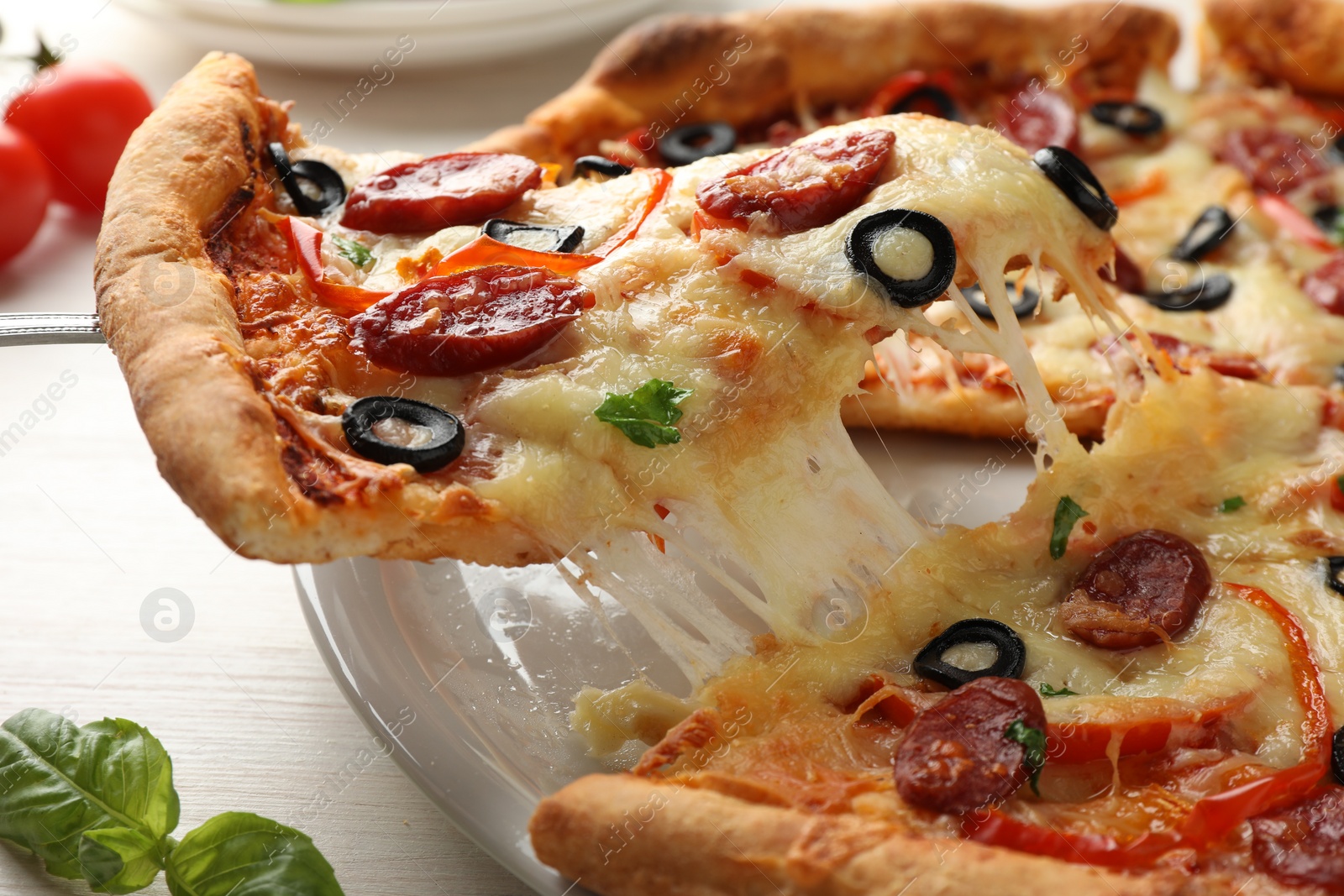 Photo of Taking piece of tasty pizza with smoked sausages, olives, pepper and parsley at light wooden table, closeup