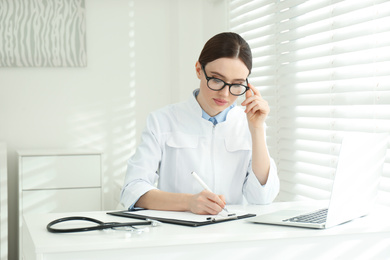 Young female doctor working at table in office