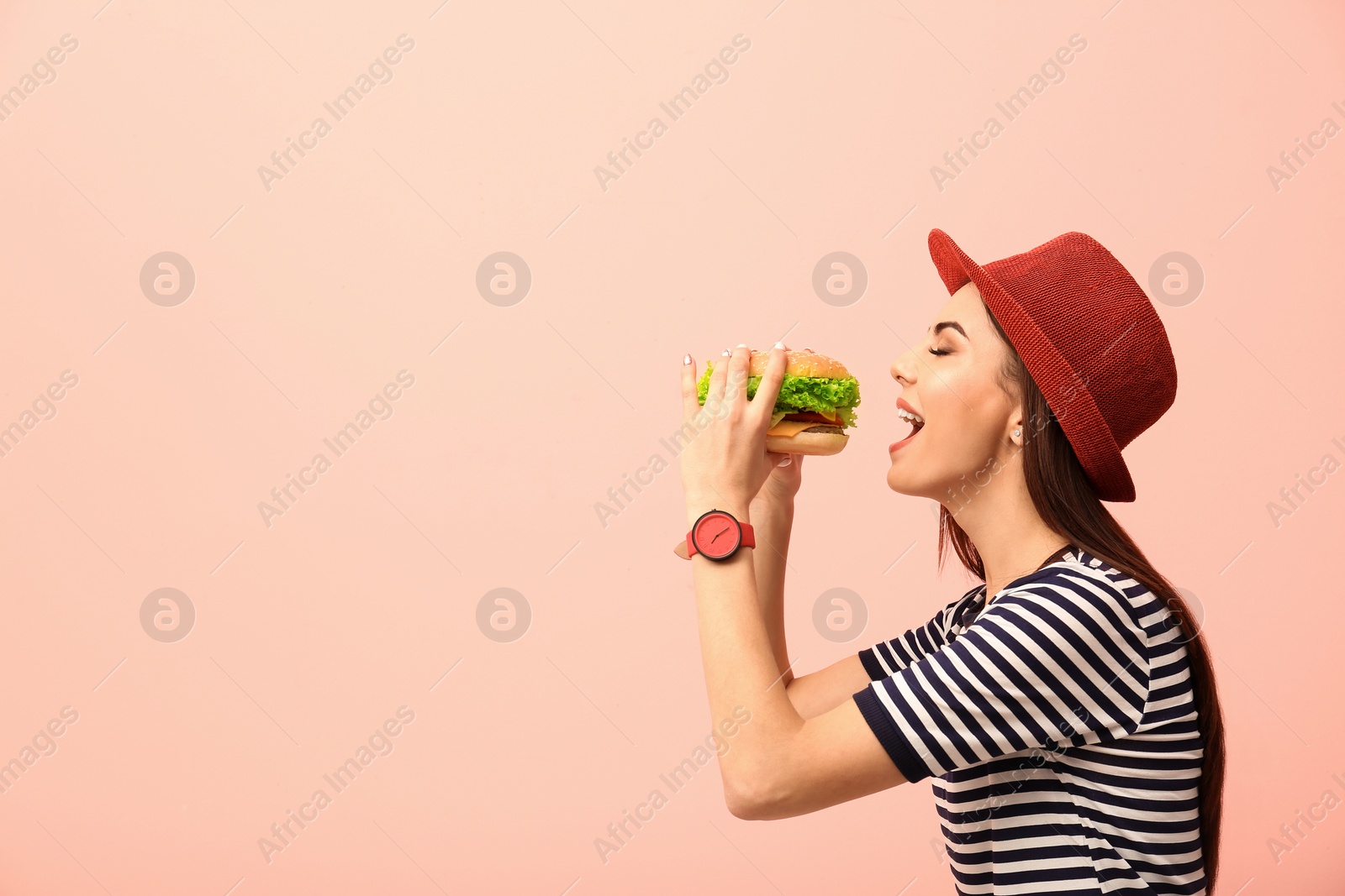 Photo of Young woman eating tasty burger on color background. Space for text