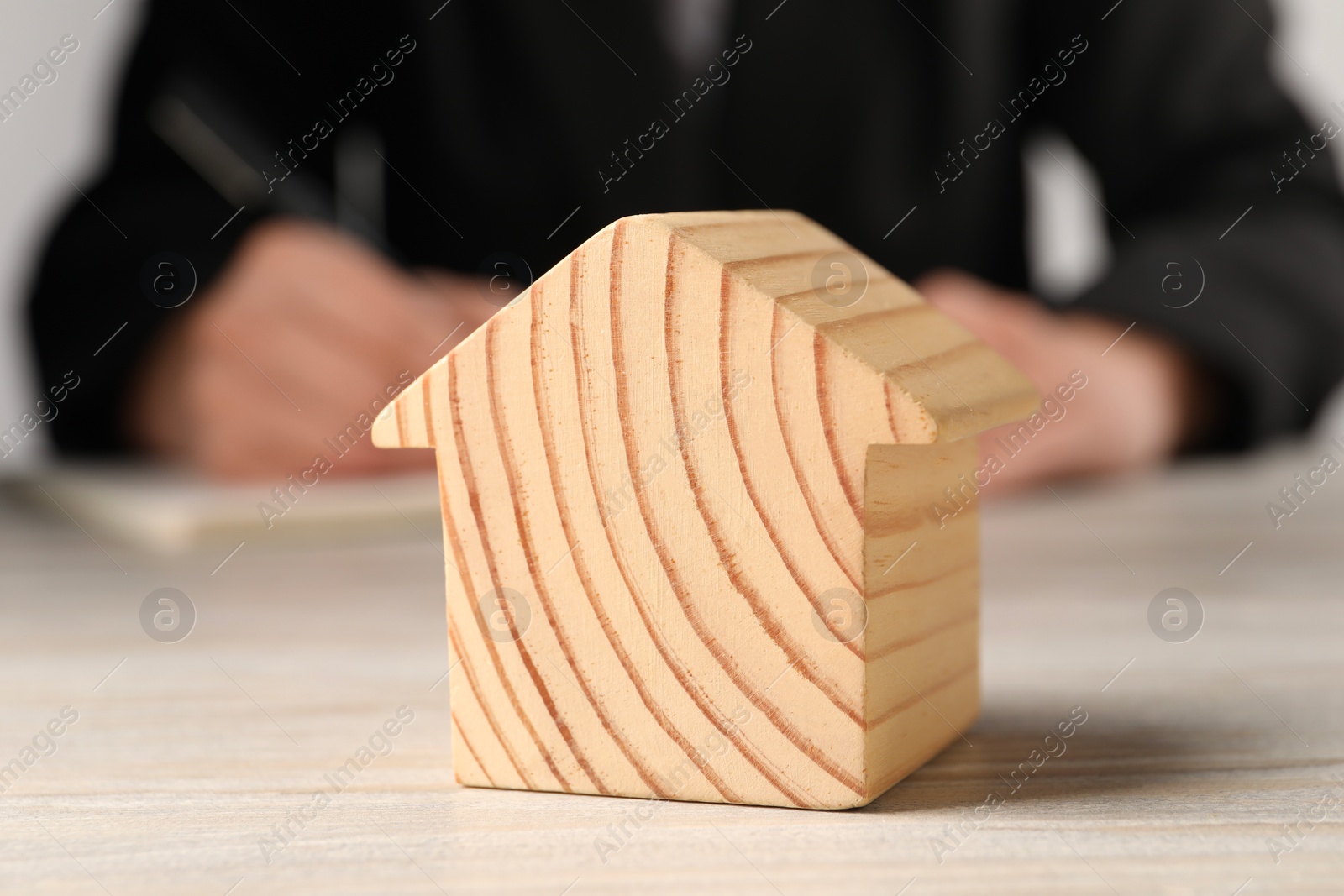 Photo of Mortgage concept. Woman writing at white wooden table, focus on house model