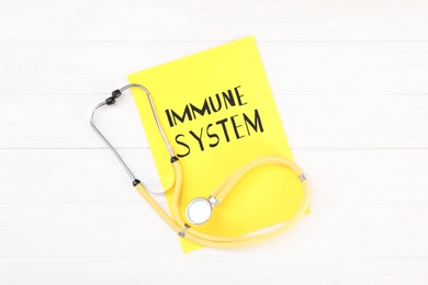 Photo of Paper sheet with text Immune System and stethoscope on white wooden table, flat lay