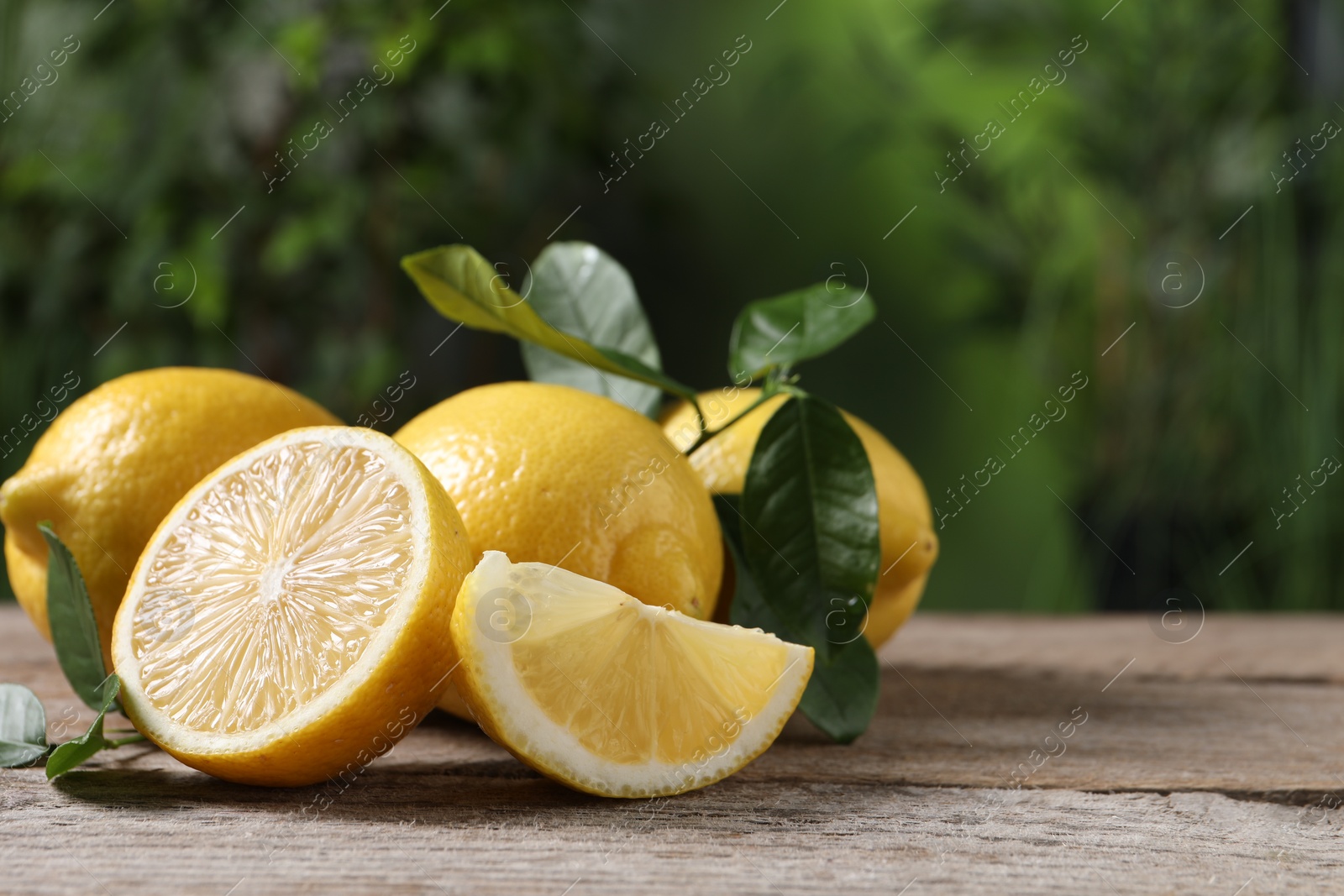 Photo of Fresh lemons and green leaves on wooden table outdoors, closeup