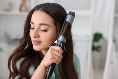 Photo of Beautiful woman using curling hair iron indoors. Space for text