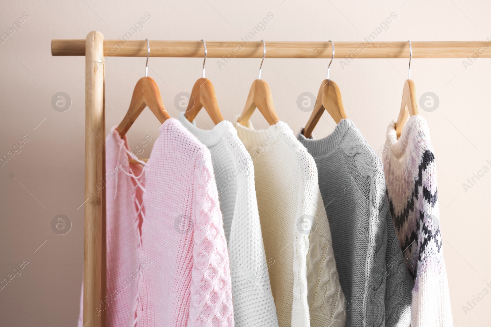 Photo of Collection of warm sweaters hanging on rack near light wall