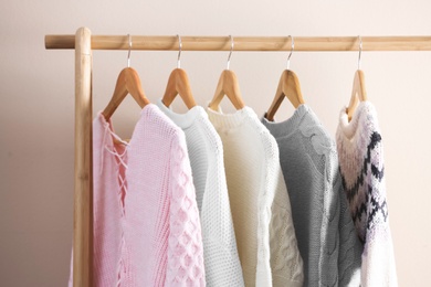 Photo of Collection of warm sweaters hanging on rack near light wall