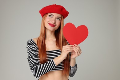 Young woman with paper heart on light grey background