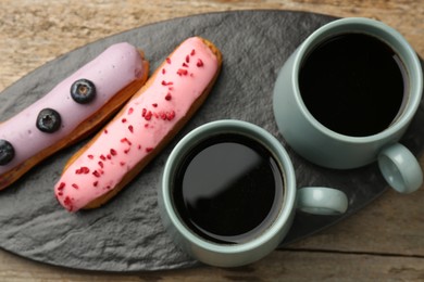 Aromatic coffee in cups and tasty eclairs on wooden table, top view