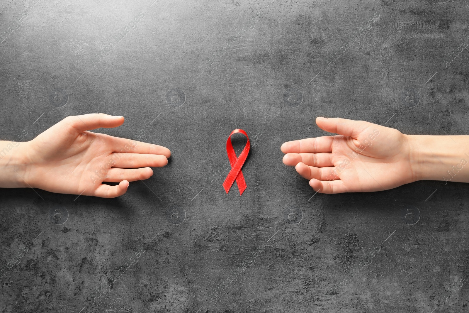 Photo of Women reaching for red ribbon on grey background, top view. Cancer awareness