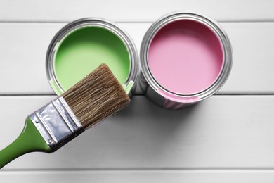 Cans of pink and green paints with brush on white wooden table, flat lay