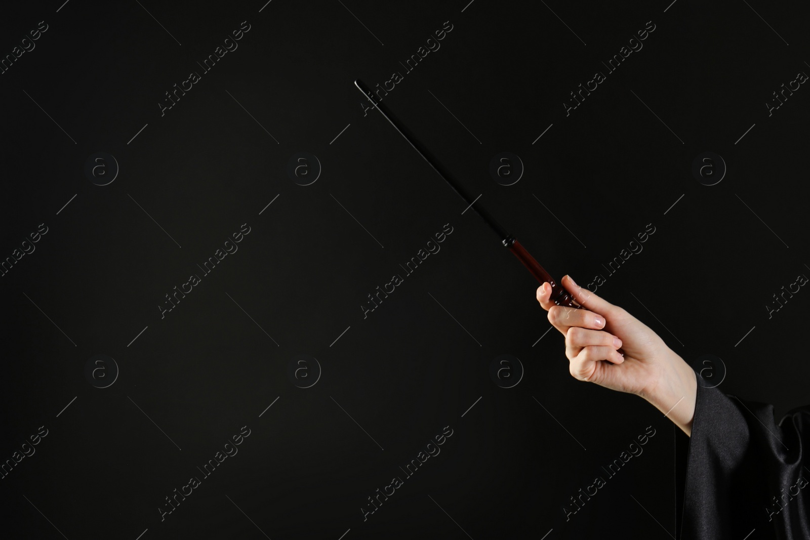 Photo of Wizard holding magic wand on black background, closeup. Space for text