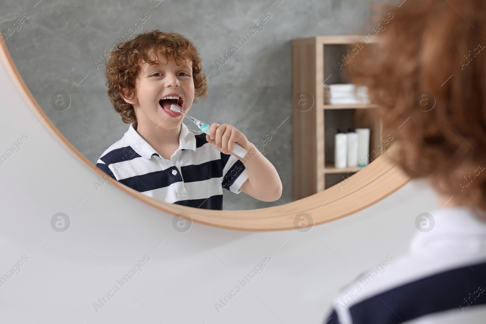 Photo of Cute little boy brushing his teeth with electric toothbrush near mirror in bathroom