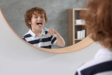 Cute little boy brushing his teeth with electric toothbrush near mirror in bathroom