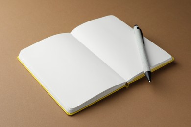 Photo of Open notebook with blank pages and pen on light brown background