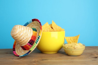 Mexican sombrero hat, nachos chips and guacamole on wooden table against light blue background