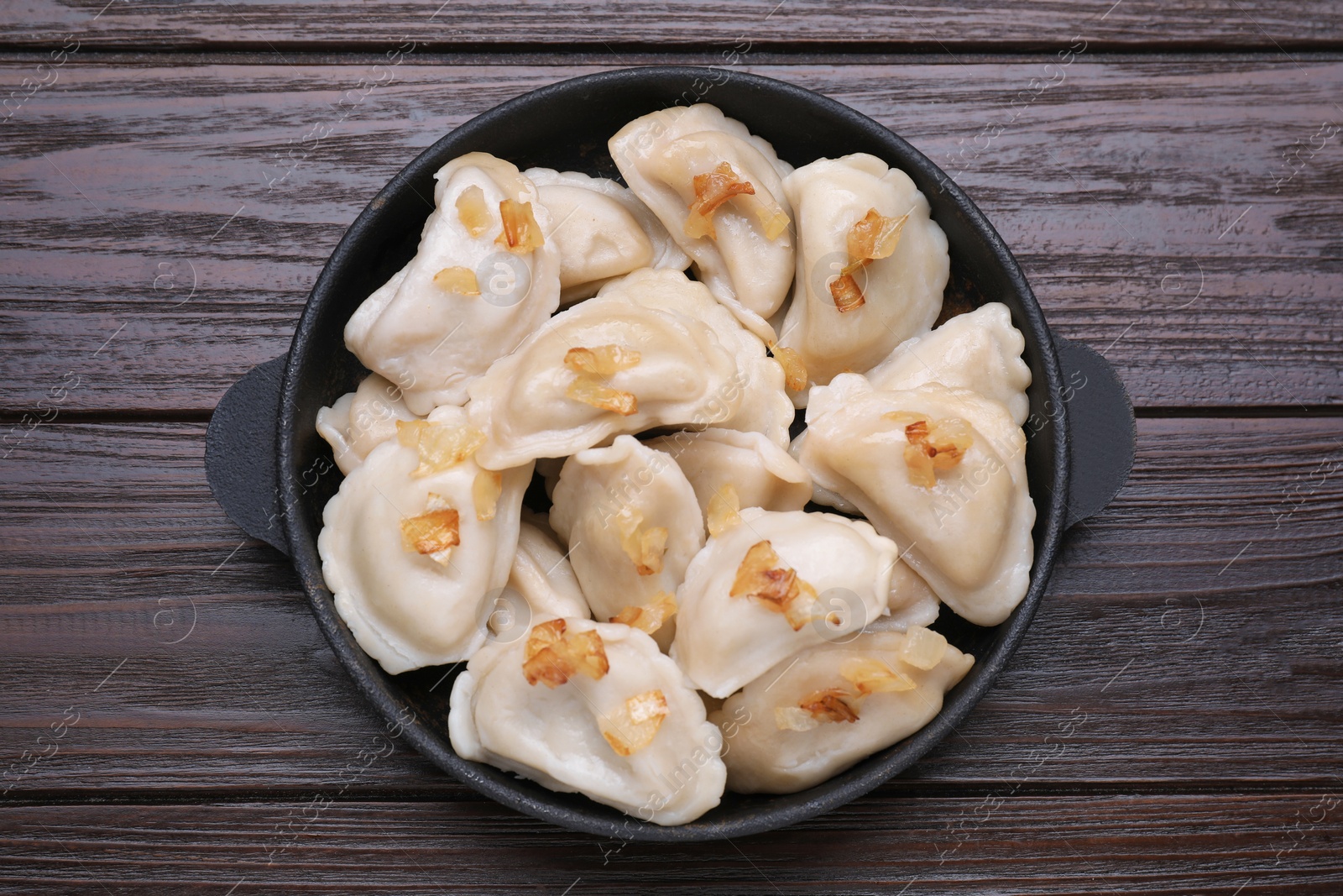 Photo of Delicious dumplings (varenyky) with potatoes and onion on brown wooden table, top view