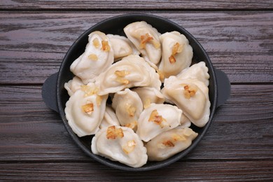 Delicious dumplings (varenyky) with potatoes and onion on brown wooden table, top view