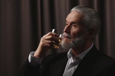 Photo of Senior man in suit drinking whiskey on brown background. Space for text