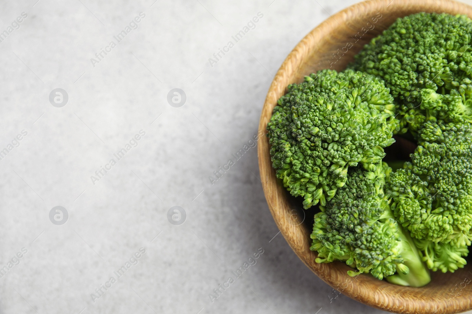 Photo of Fresh green broccoli in bowl on light table, top view. Space for text