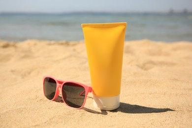 Photo of Tube of sunscreen and sunglasses on sandy beach. Sun protection care