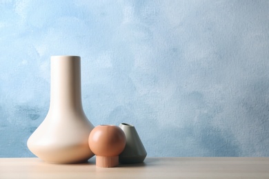 Photo of Stylish ceramic vases on wooden table against light blue background. Space for text