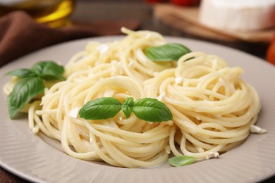 Delicious pasta with brie cheese and basil leaves on table, closeup