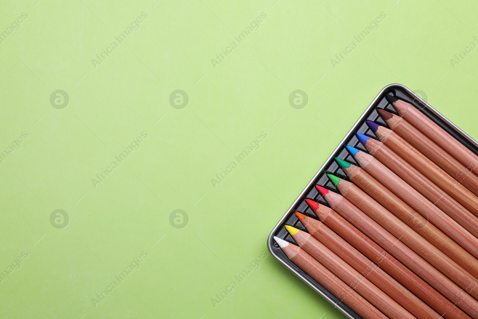 Photo of Box with many colorful pastel pencils on light green background, top view and space for text. Drawing supplies
