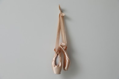 Photo of Beautiful beige ballet shoes with cute ribbons hanging on light grey wall