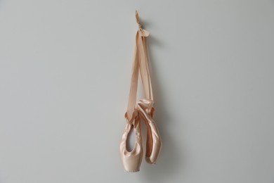 Beautiful beige ballet shoes with cute ribbons hanging on light grey wall