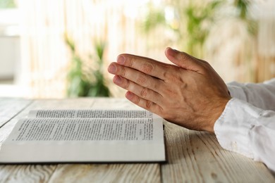 Photo of Man with Bible praying at white wooden table indoors, closeup