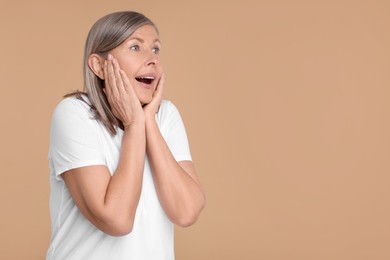 Portrait of surprised senior woman on beige background, space for text