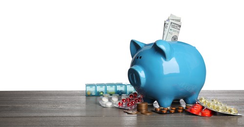 Photo of Piggy bank with money and pills on wooden table against white background, space for text. Medical insurance