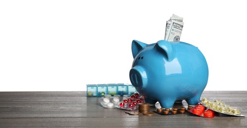 Piggy bank with money and pills on wooden table against white background, space for text. Medical insurance