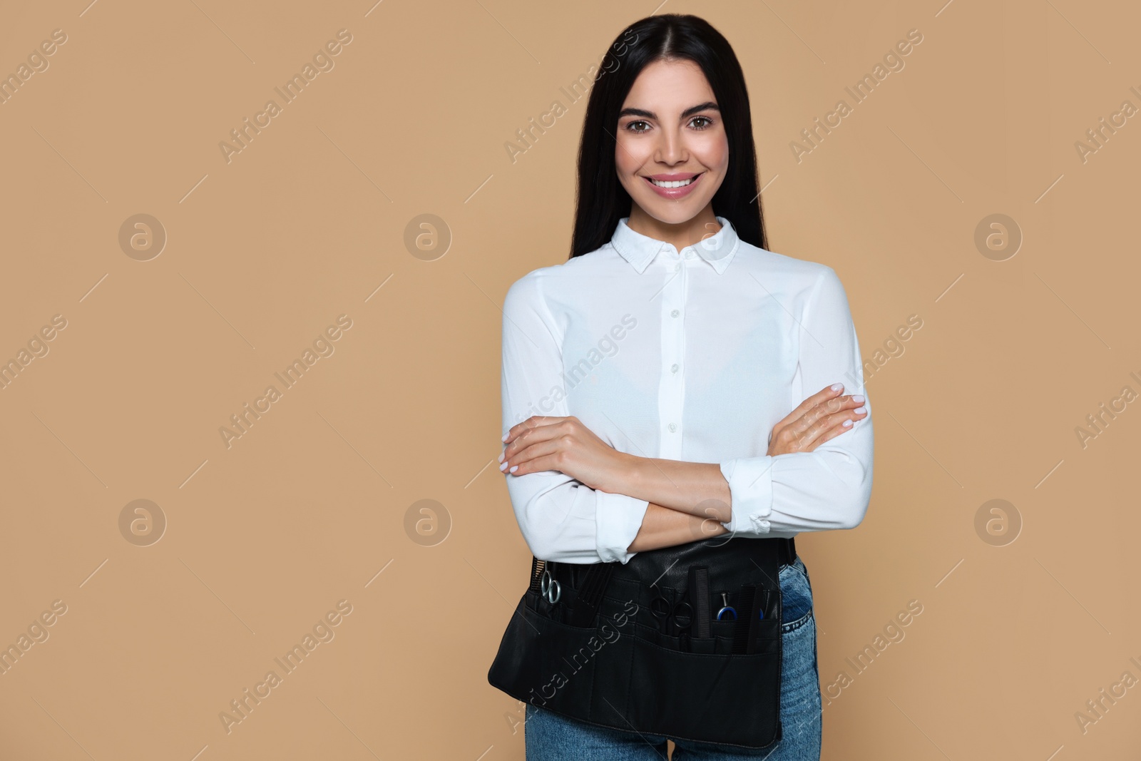 Photo of Portrait of happy hairdresser with professional tools on beige background, space for text