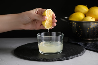 Photo of Woman squeezing lemon juice into glass bowl at grey table, closeup