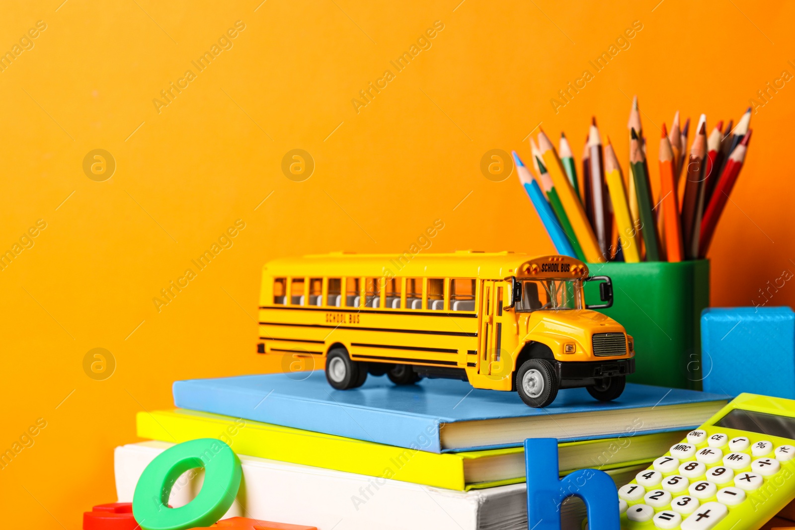 Photo of School bus model and stationery on orange background. Transport for students