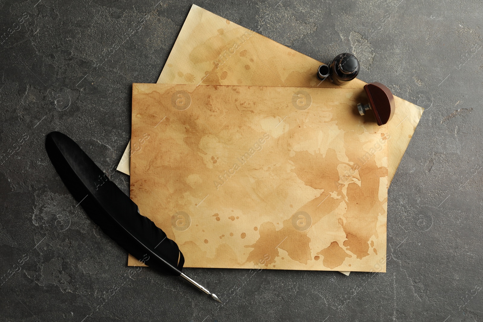 Photo of Black feather, inkwell and vintage parchment on grey table, flat lay