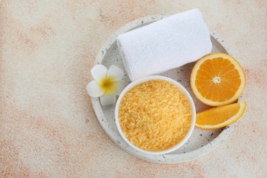 Sea salt, towel, plumeria flower and cut orange on beige textured table, top view. Space for text