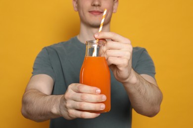 Photo of Young man with glass of juice on orange background, closeup