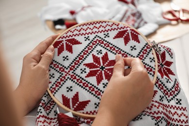 Photo of Woman embroidering white shirt with colorful threads in hoop, closeup. Ukrainian national clothes