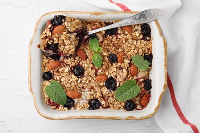 Photo of Tasty baked oatmeal with berries and almonds in baking tray on white textured table, top view