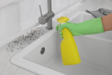 Woman in rubber gloves using mold remover on countertop in kitchen, closeup