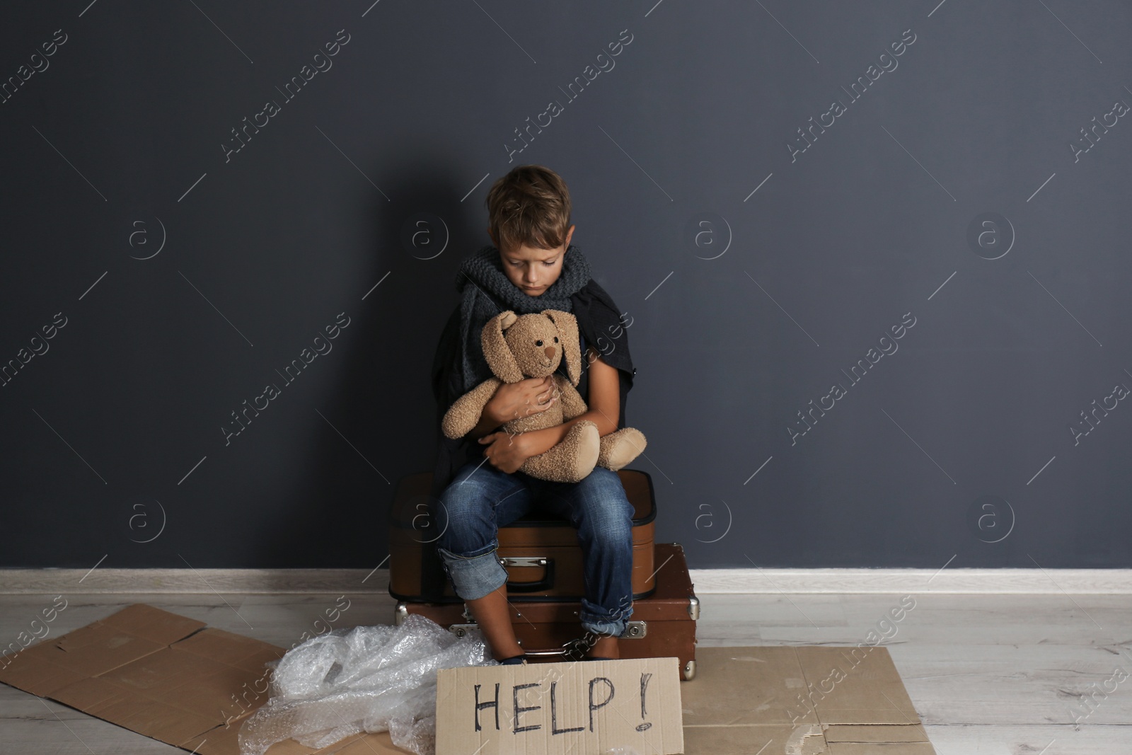 Photo of Poor boy with toy asking for help near dark wall