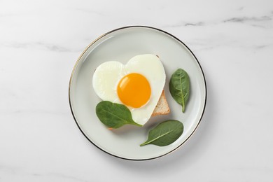 Photo of Romantic breakfast with heart shaped fried egg on white marble table, top view