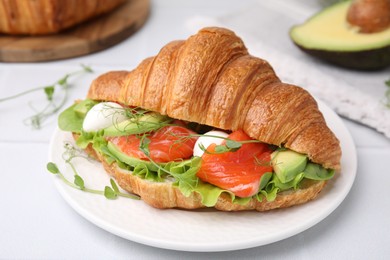 Tasty croissant with salmon, avocado, mozzarella and lettuce on white table, closeup