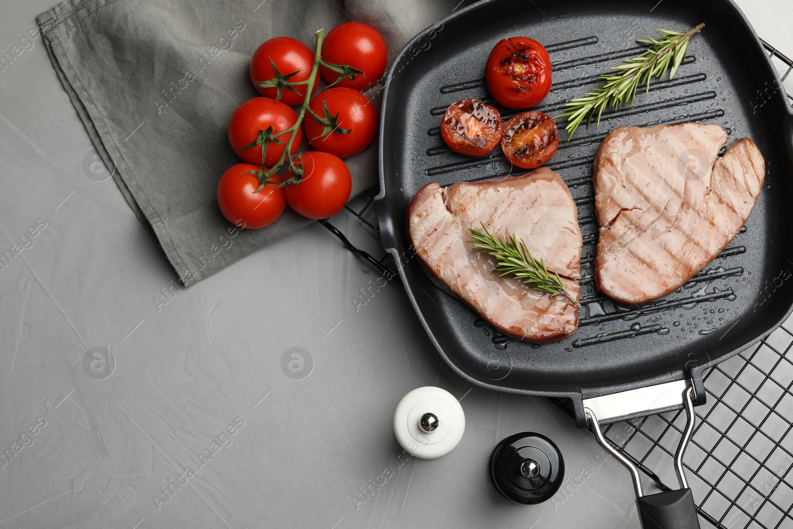 Photo of Delicious tuna steaks with rosemary and tomatoes on grey table, flat lay. Space for text