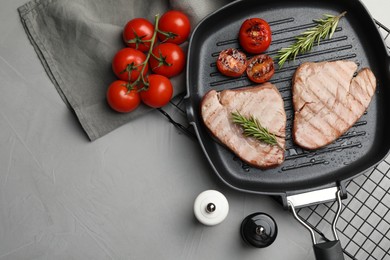 Delicious tuna steaks with rosemary and tomatoes on grey table, flat lay. Space for text