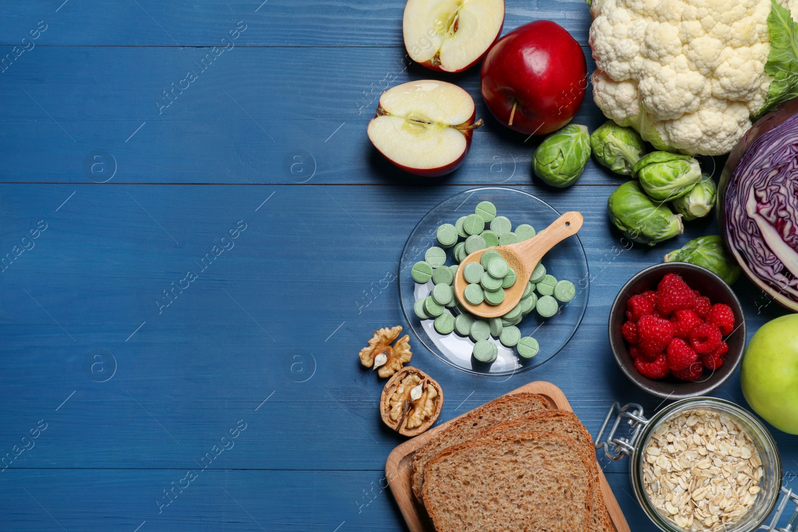 Photo of Bowl with pills, foodstuff and space for text on blue wooden table, flat lay. Prebiotic supplements