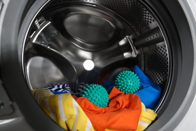 Photo of Green dryer balls and clothes in washing machine drum, closeup