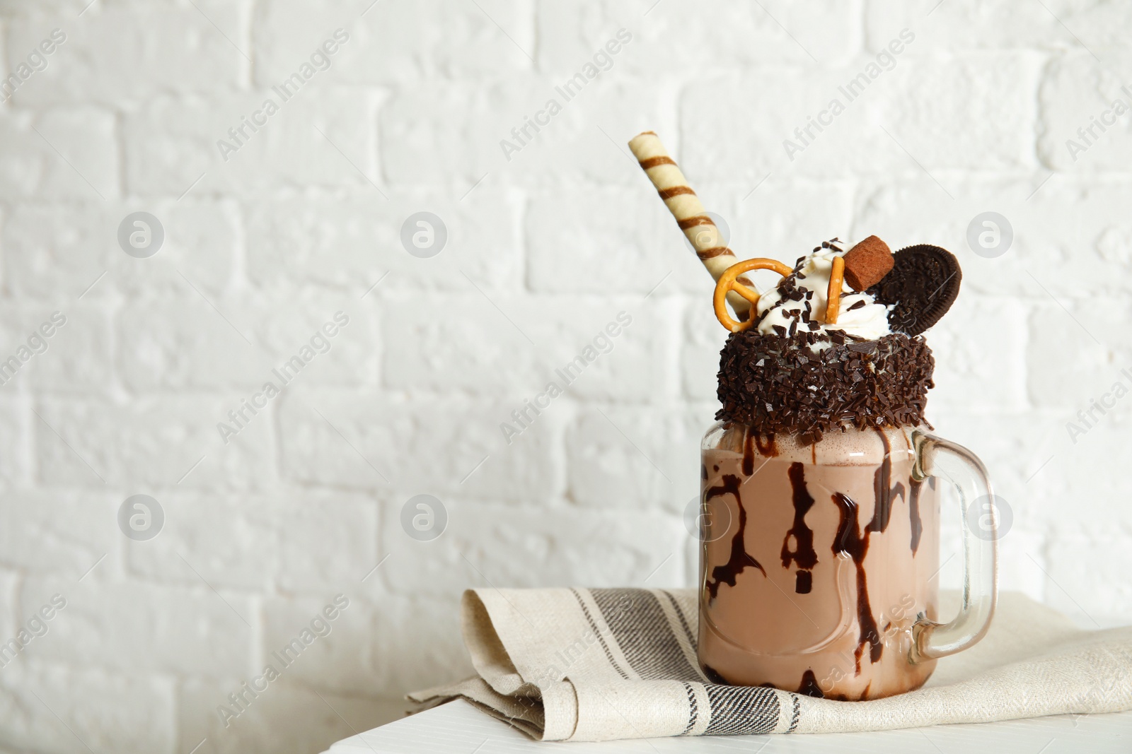 Photo of Mason jar of tasty milk shake with sweets on table near brick wall. Space for text